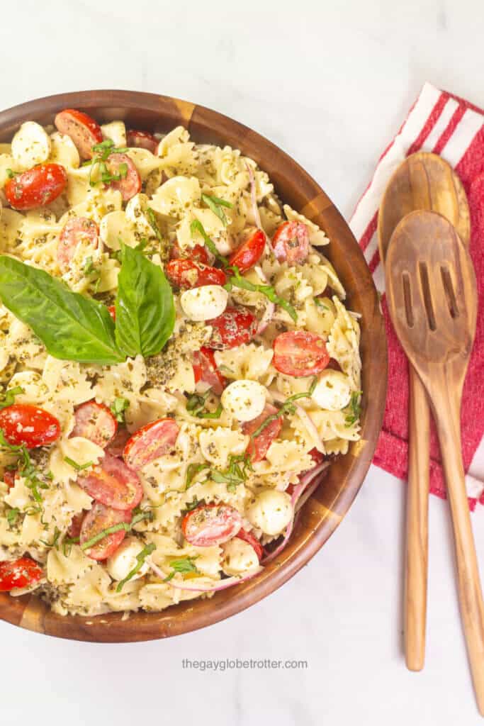 Caprese pesto pasta salad in a wood serving bowl with wooden salad spoons.