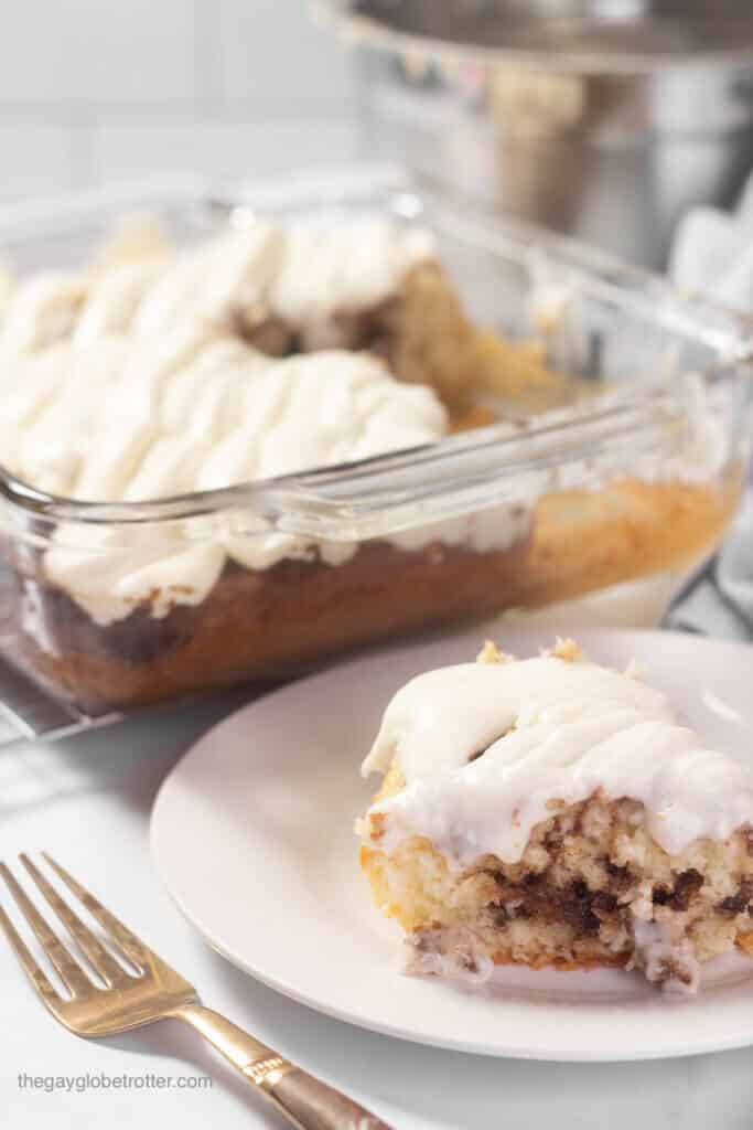 A plate of cinnamon roll cake next to a baking pan and a fork.