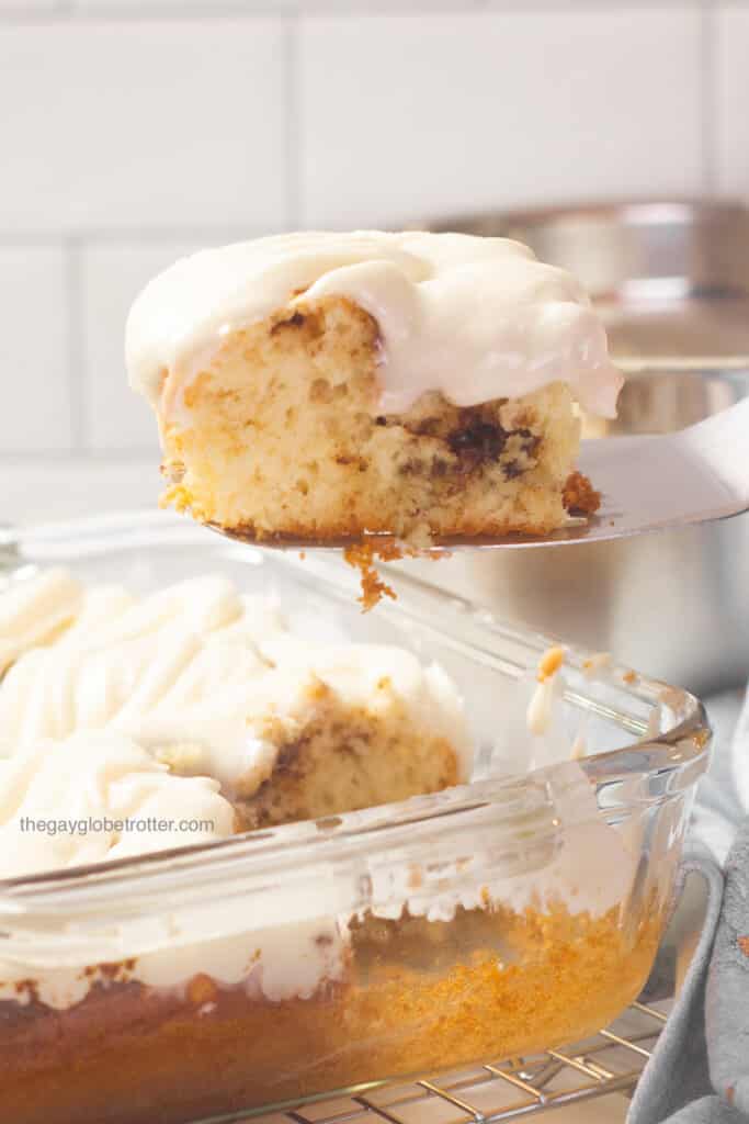 A spatula lifting cinnamon roll cake out of a clear baking dish.