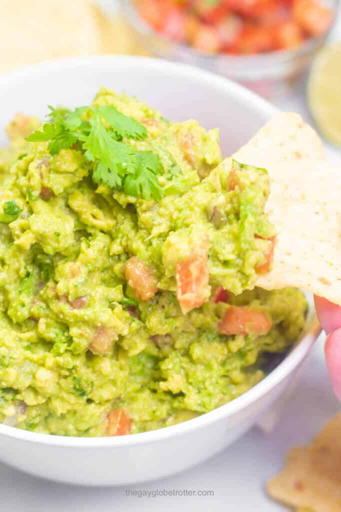 A tortilla chip scooping fresh guacamole out of a serving bowl.