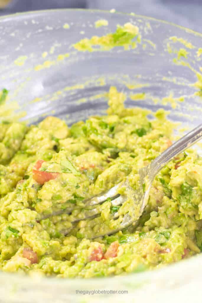 A fork mashing guacamole ingredients like avocados and tomatoes.