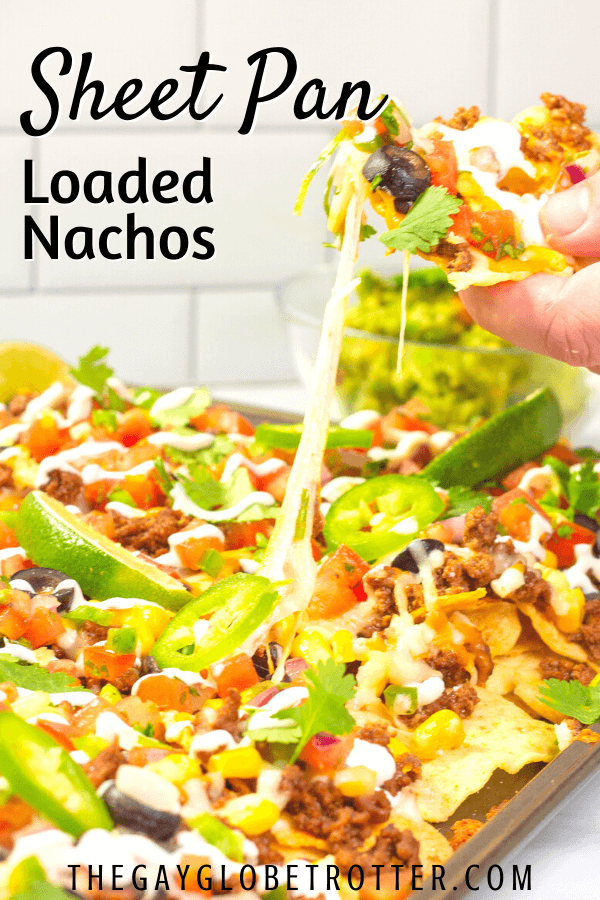 A hand grabbing a loaded nacho from a tray with text overlay that says "sheet pan loaded nachos".