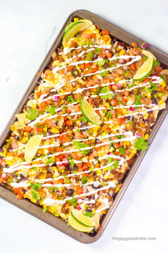 A baking sheet of loaded nachos topped with lime wedges, sour cream, and cilantro.