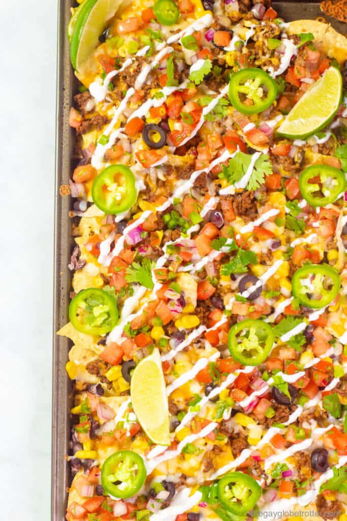 A close up of nacho toppings like sour cream, lime wedges, jalapenos, and green onions.
