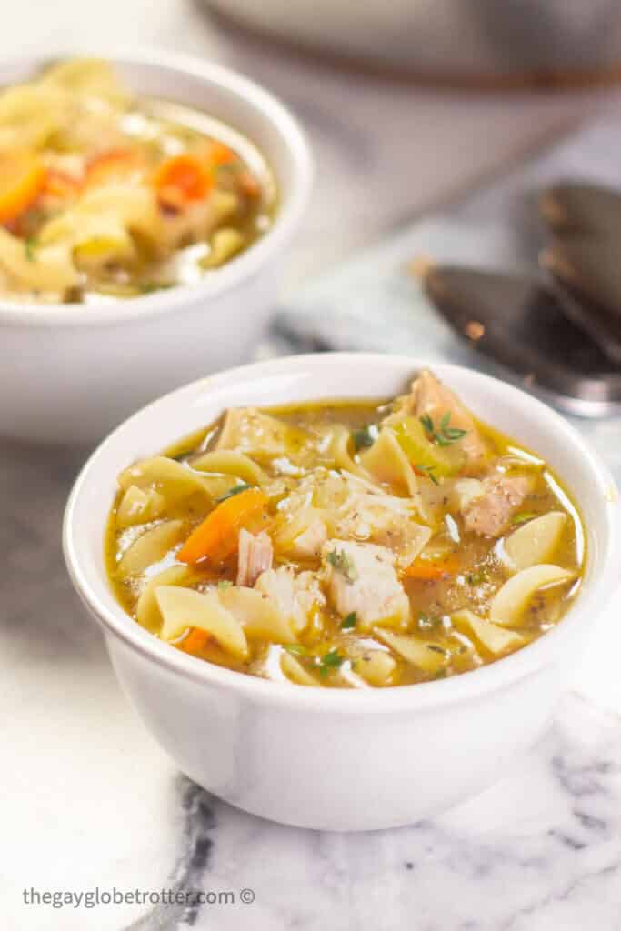 A bowl of turkey noodle soup next to a spoon.