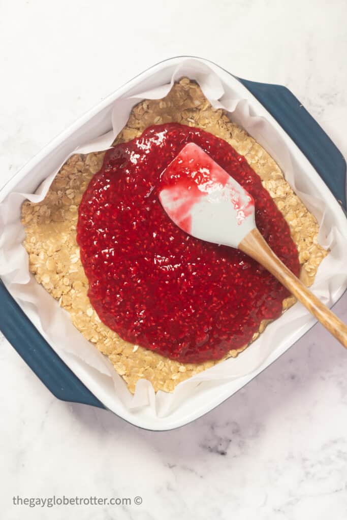 Raspberry sauce being spread on an oatmeal layer.