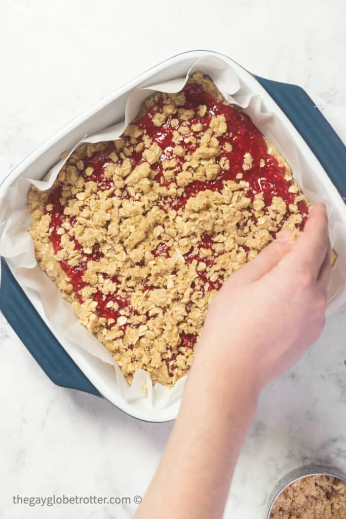 Oatmeal streusel being sprinkled on the raspberry layer.