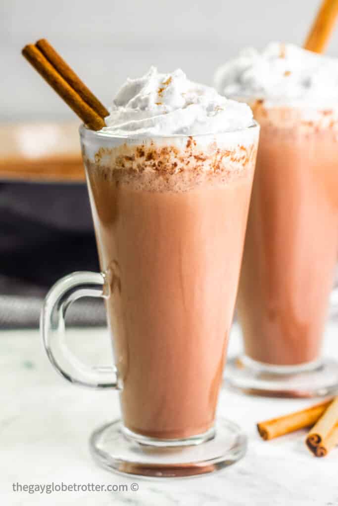 A cup of Mexican hot chocolate garnished with cinnamon sticks and whipped cream.