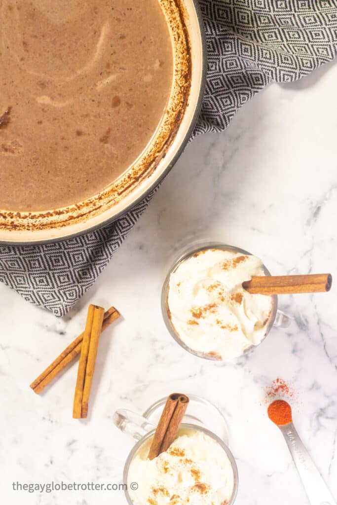 A pot of mexican hot chocolate next to cinnamon sticks.