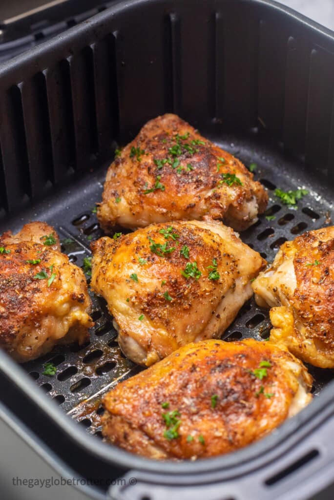An air fryer basket filled with cooked crispy chicken thighs.