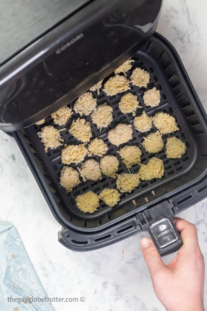 Breaded pickles being placed into the air fryer.