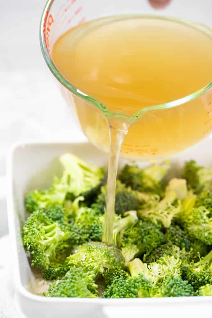 Chicken broth being poured over rice and broccoli.