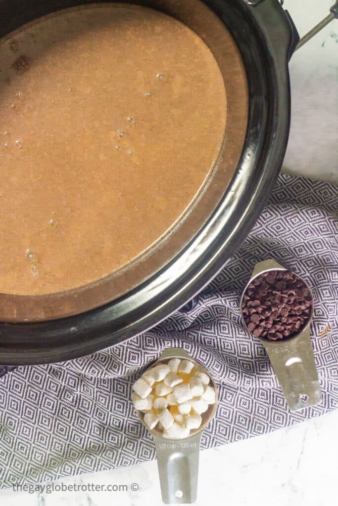 A CrockPot filled with slow cooker hot chocolate next to a tea towel.