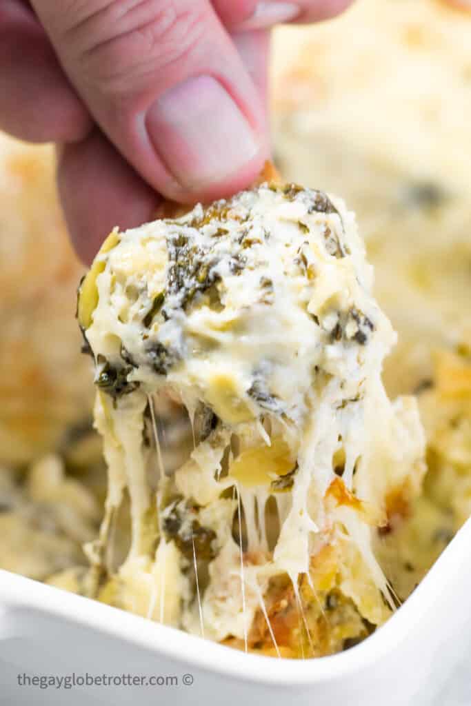 A crostini being dipped into hot spinach artichoke dip.