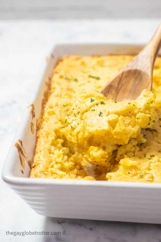 A serving spoon serving jiffy corn casserole out of a baking dish.