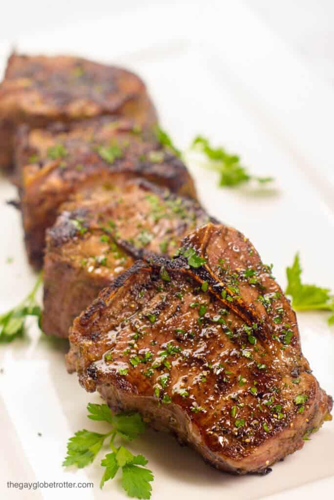 Pan seared lamb loin chops arranged on a serving plate garnished with parsley.