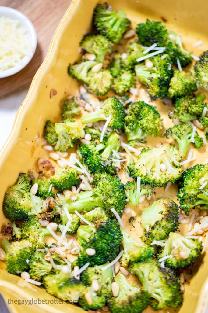 Parmesan roasted broccoli in a yellow casserole dish with pine nuts.