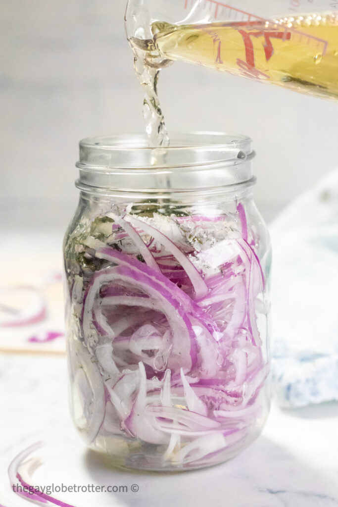 Apple cider vinegar being poured over red onions.