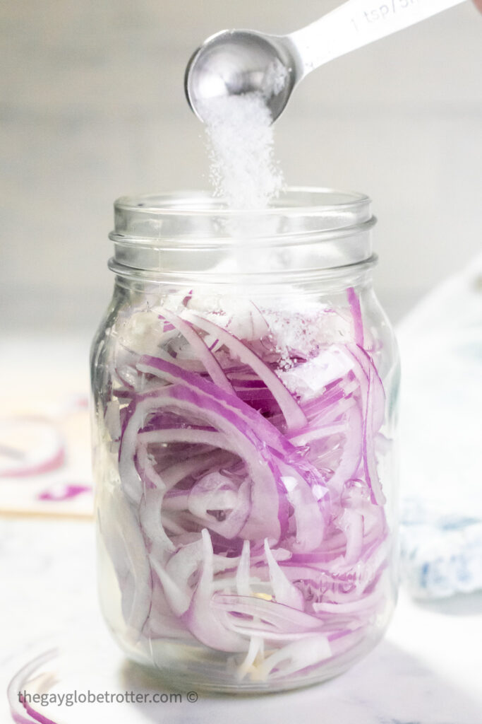 Salt being poured into a mason jar with red onions.