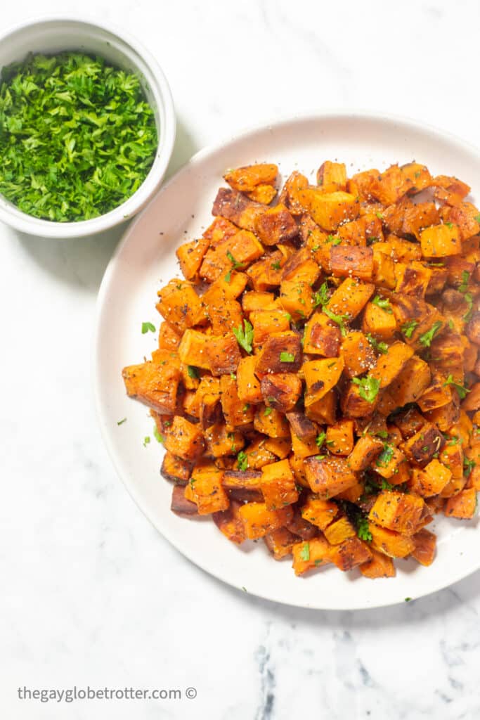 A plate of roasted sweet potatoes next to a bowl of parsley.