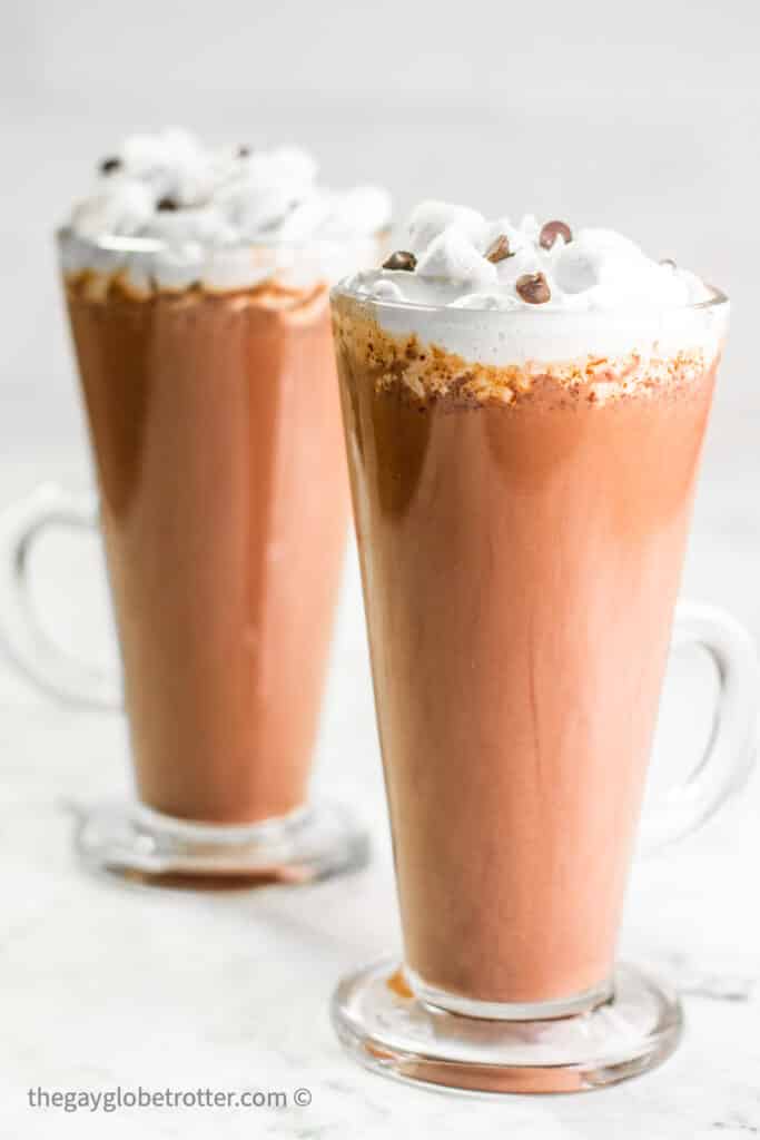 Two glasses of hot chocolate with chocolate chips and whipped cream.