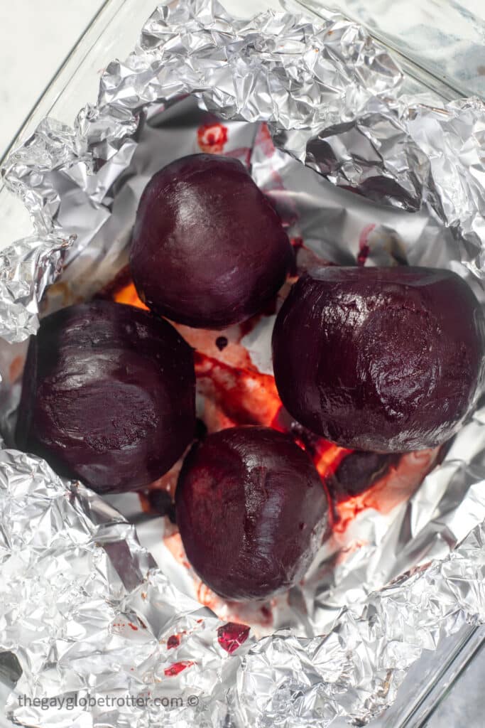 Peeled whole roasted beets in foil in a clear baking dish.