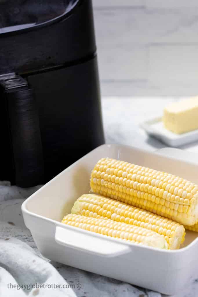 Raw corn in a dish next to an air fryer.