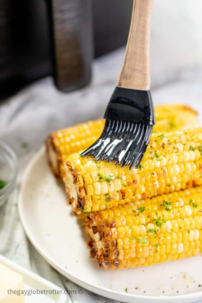 Butter being brushed onto corn on the cob.