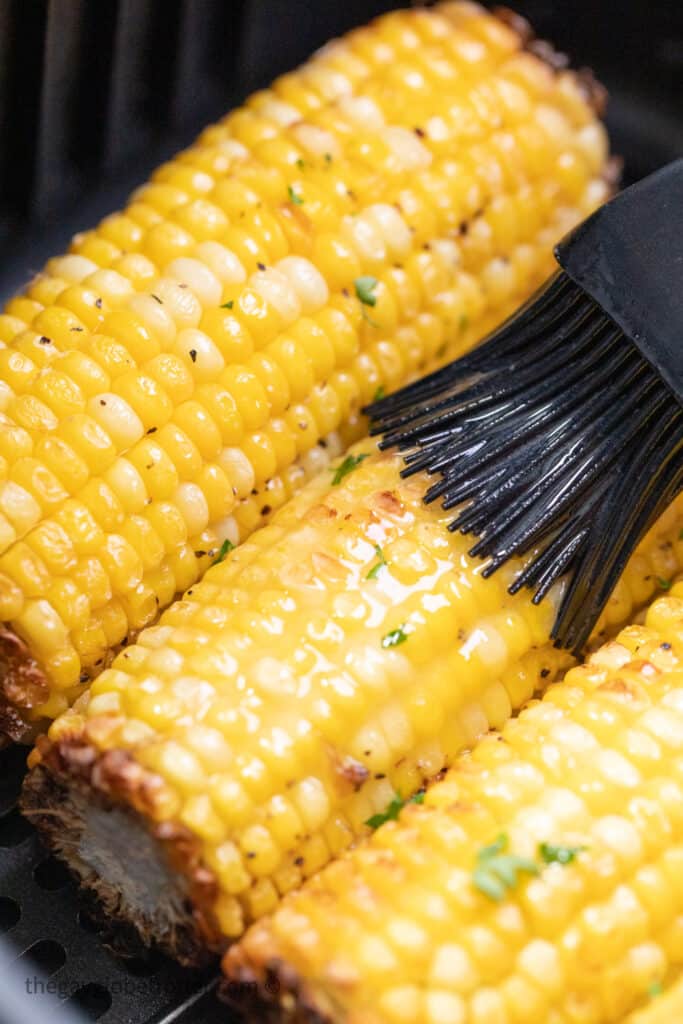Butter bing brushed on corn in the air fryer.