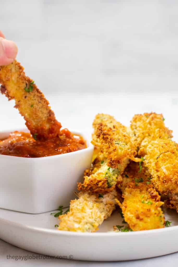 A zucchini fry being dipped into marinara sauce.