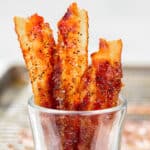 Candied bacon in a clear cup.