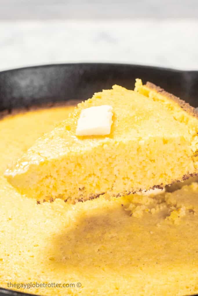 Cornbread topped with butter being served out of a cast iron skillet.