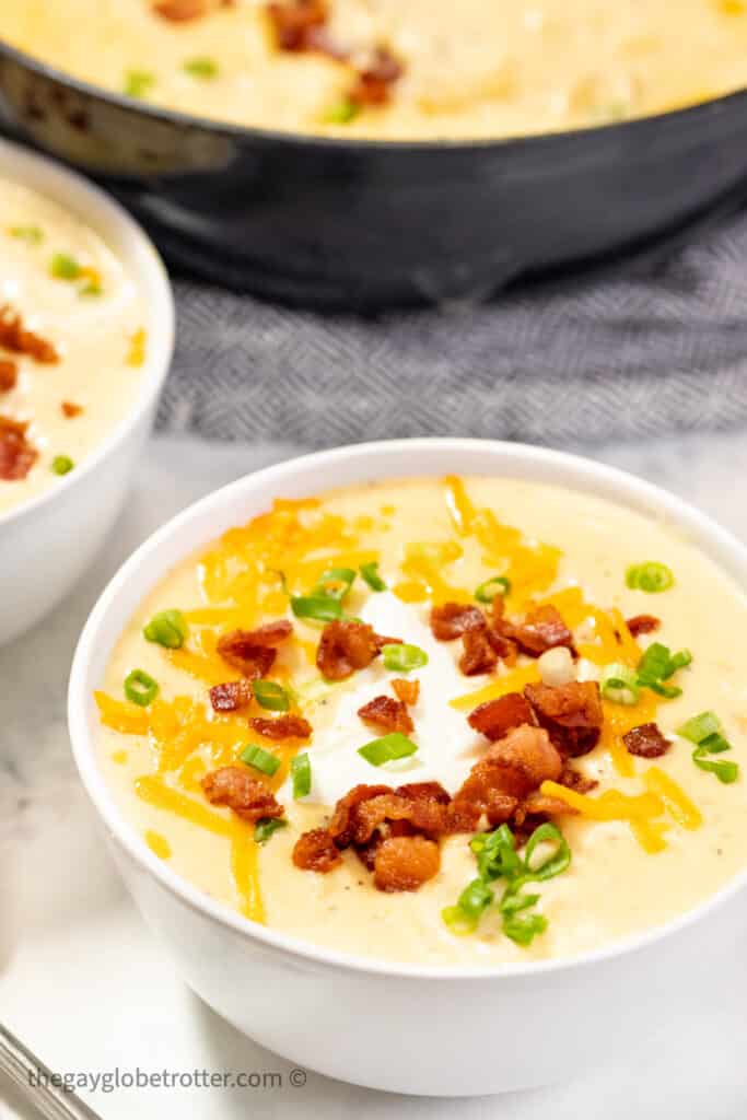 A bowl of baked potato soup garnished with bacon, cheddar cheese, and chives.