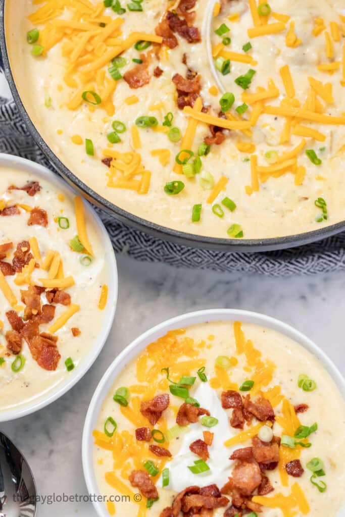 Two bowls of potato soup next to a dutch oven.