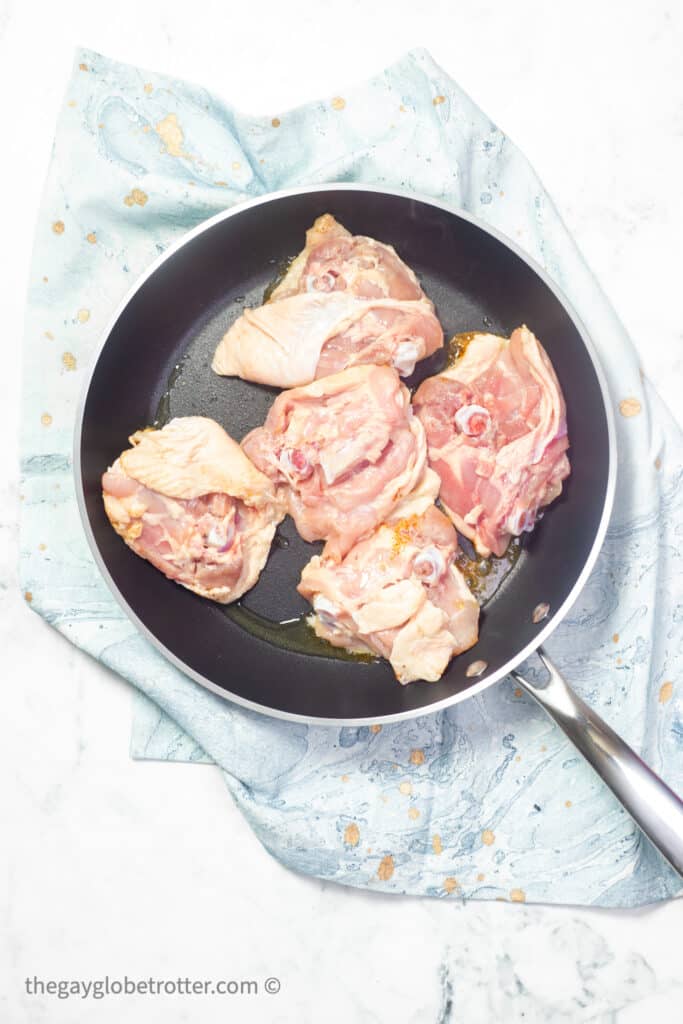 Chicken thighs being seared in a pan with skin side down.