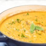 Root vegetable soup in a pot garnished with sage.