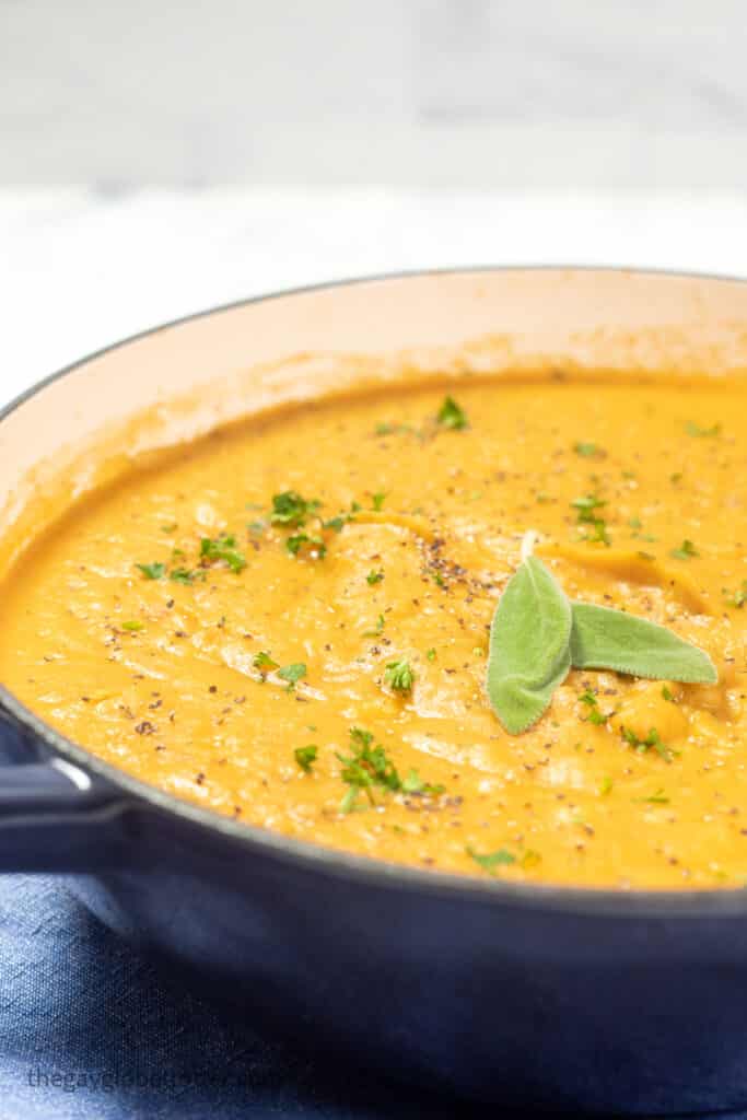 A pot of roasted root vegetable soup garnished with sage.