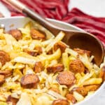 Cabbage and sausage in a skillet with a serving spoon.