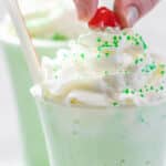 A hand placing a cherry on a shamrock shake.