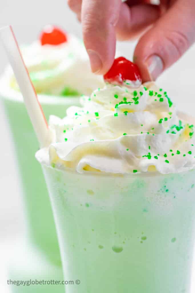 A cherry being placed on a shamrock shake.