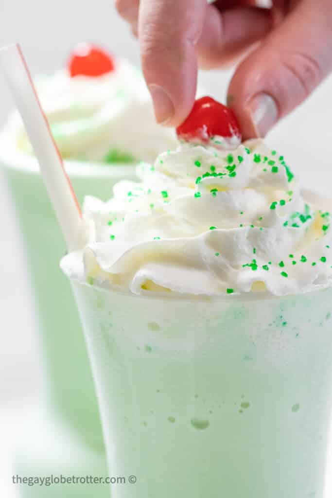 A hand placing a cherry on a shamrock shake.