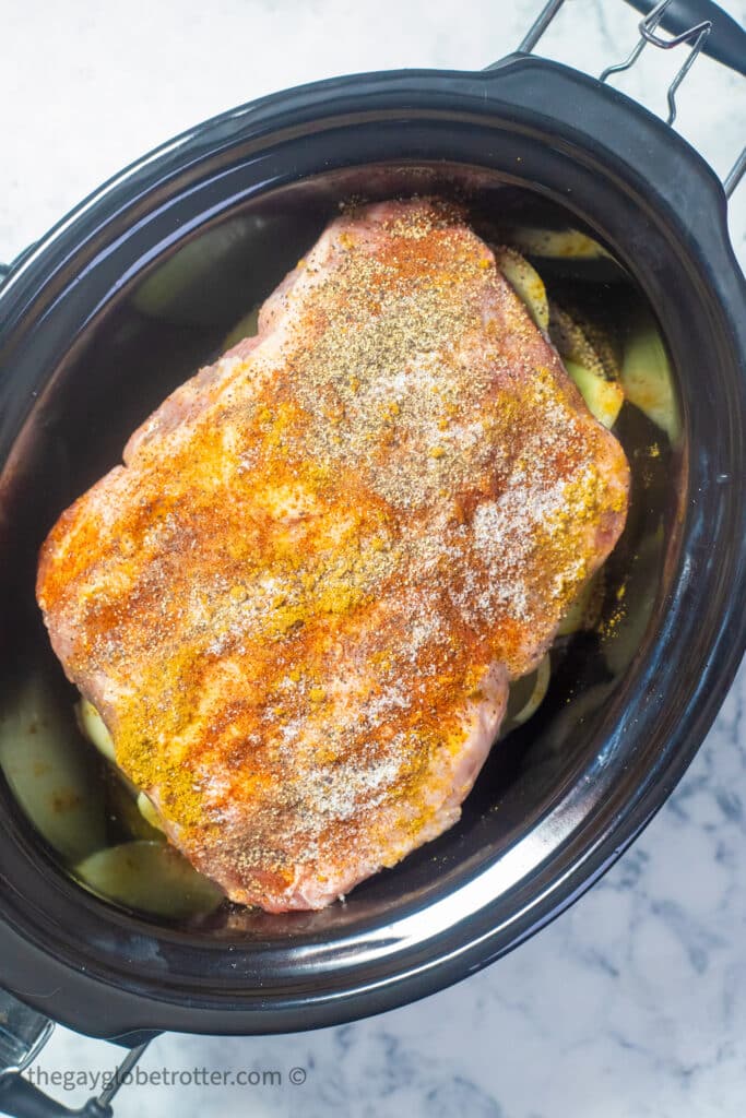 Pork shoulder roast in a slow cooker with spices.