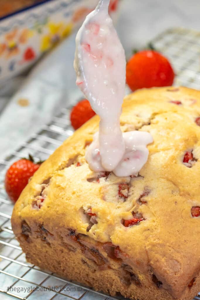 A spoon drizzling strawberry glaze on a loaf of strawberry bread.