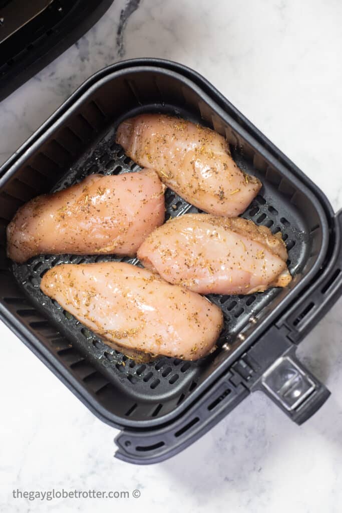 Raw chicken breasts in an air fryer basket.