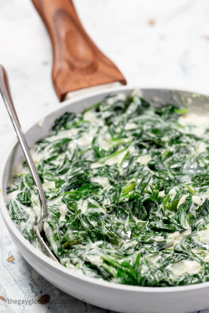 A spoon serving creamed spinach from a saucepan.