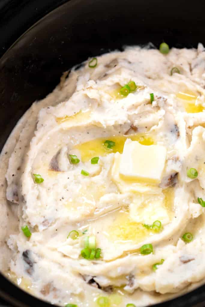 Butter and chives on mashed potatoes in a slow cooker.