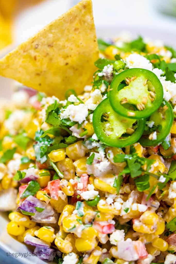 Mexican street corn dip garnished with a tortilla chip and jalapenos.