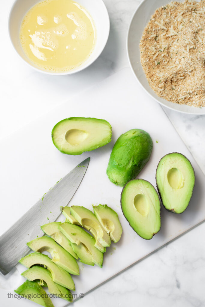 Avocados being cut next to breadcrumbs and egg mixture.