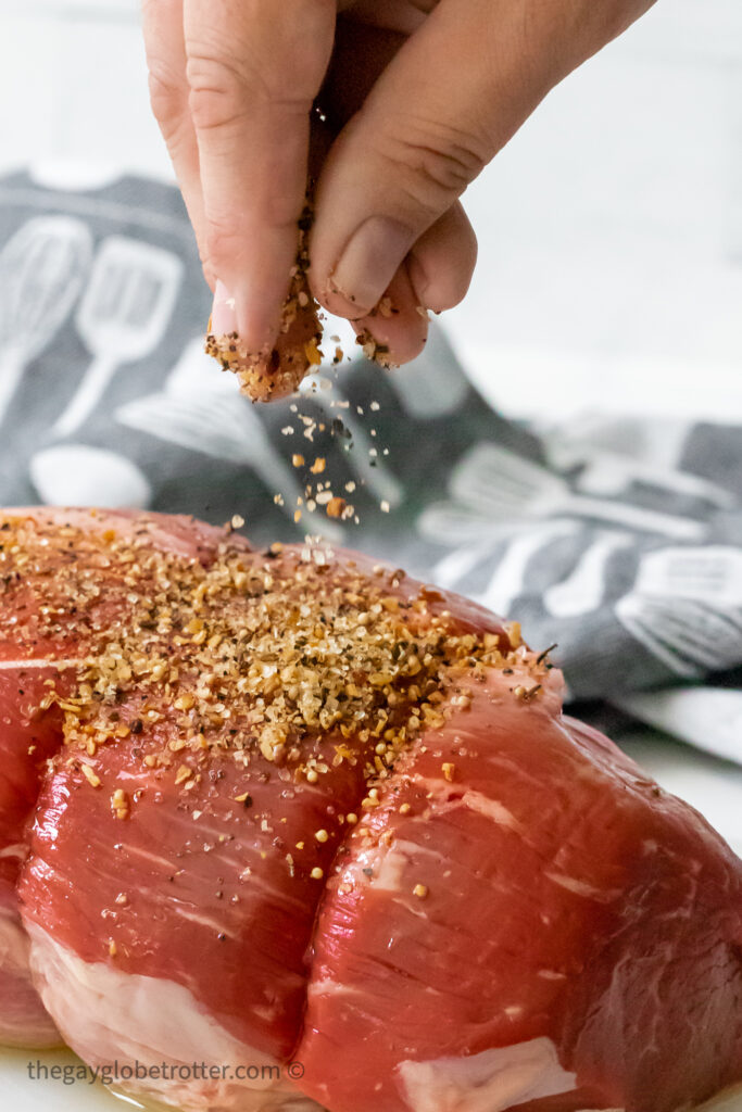 A hand sprinkling montreal steak spice on a roast.