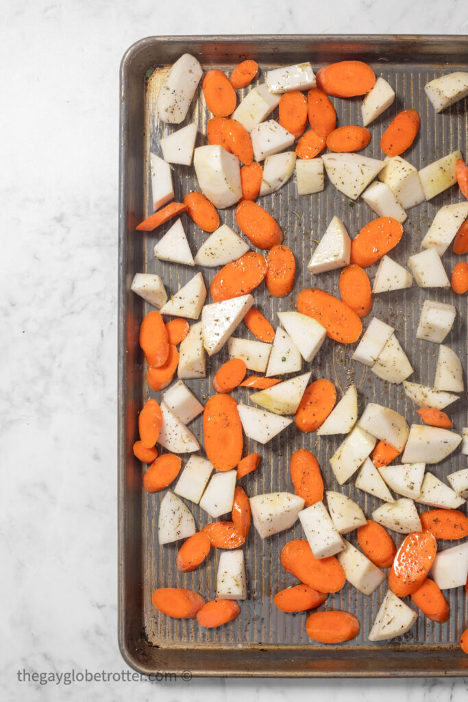 Carrots and turnips on a baking sheet with seasonings.
